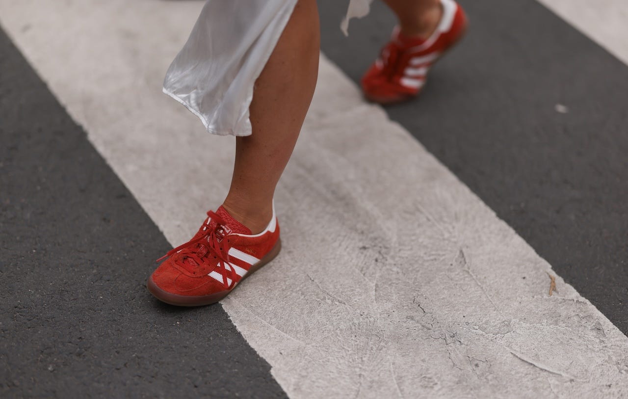 A person walks a street in Paris wearing red Adidas sambas.