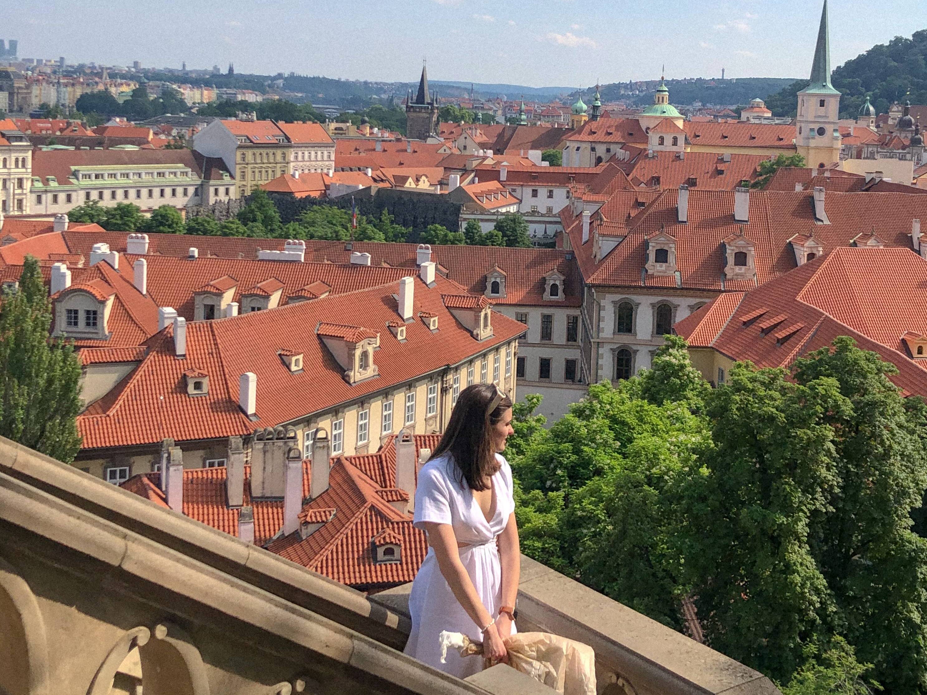 A girl in a white dress poses with Prague in the background