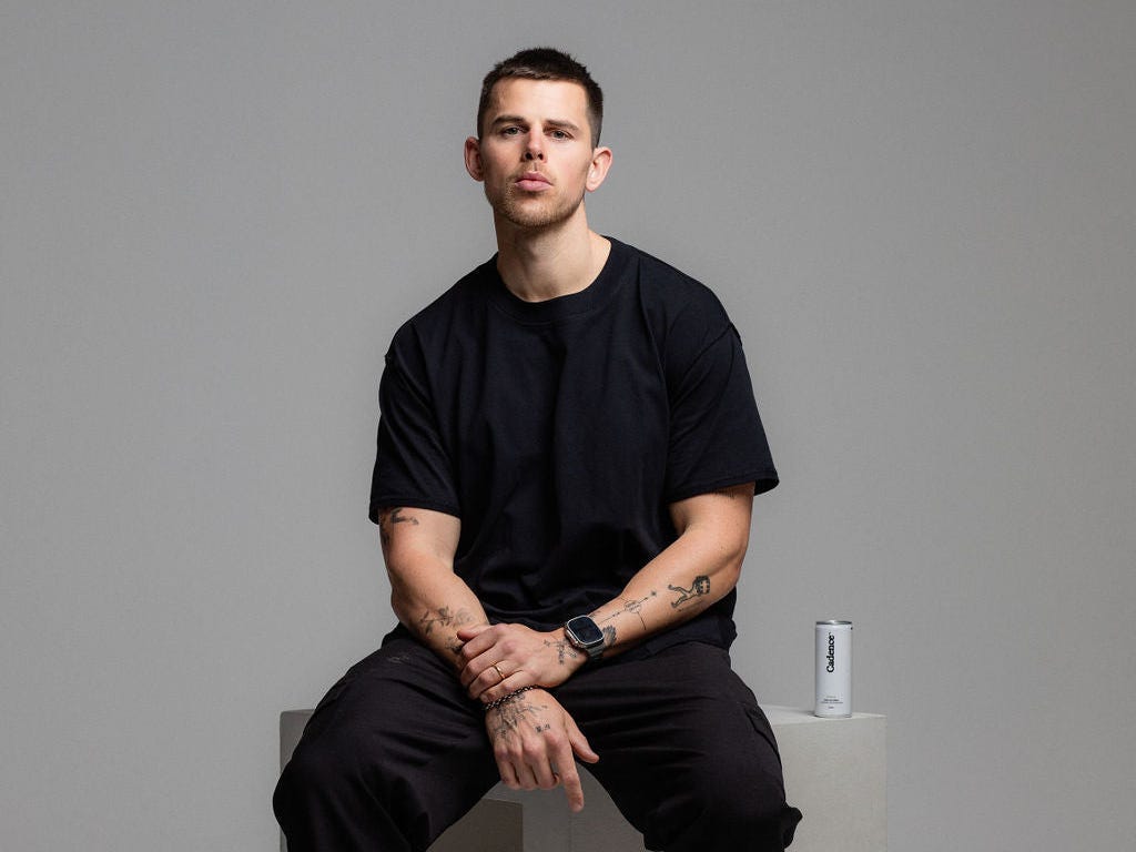 a man in an all-black outfit sits in front of a gray background