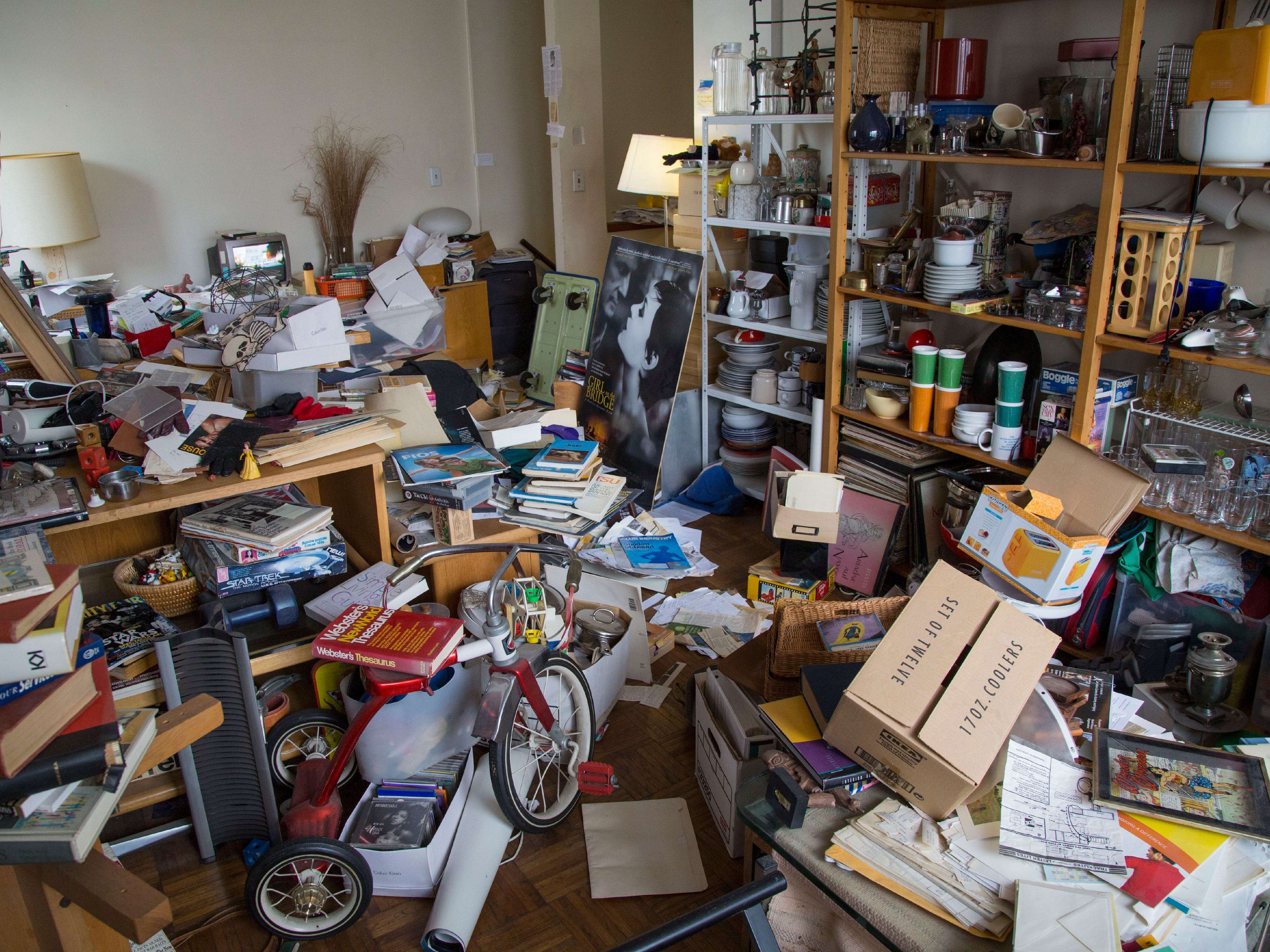 A room packed with clutter, including books, lamps, a child's tricycle, and photo frames.