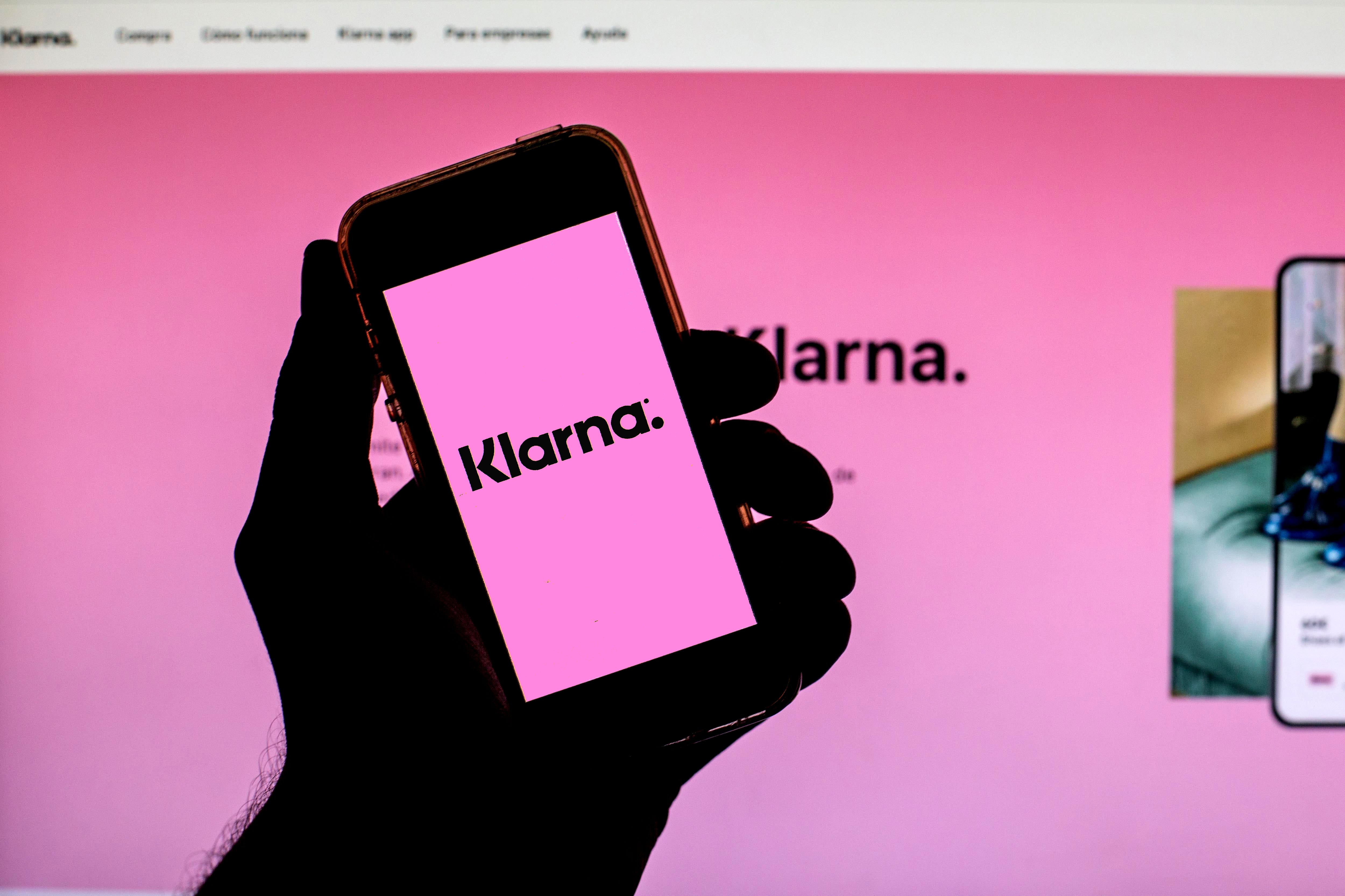 Klarna's logo displayed on a phone screen with its website behind it