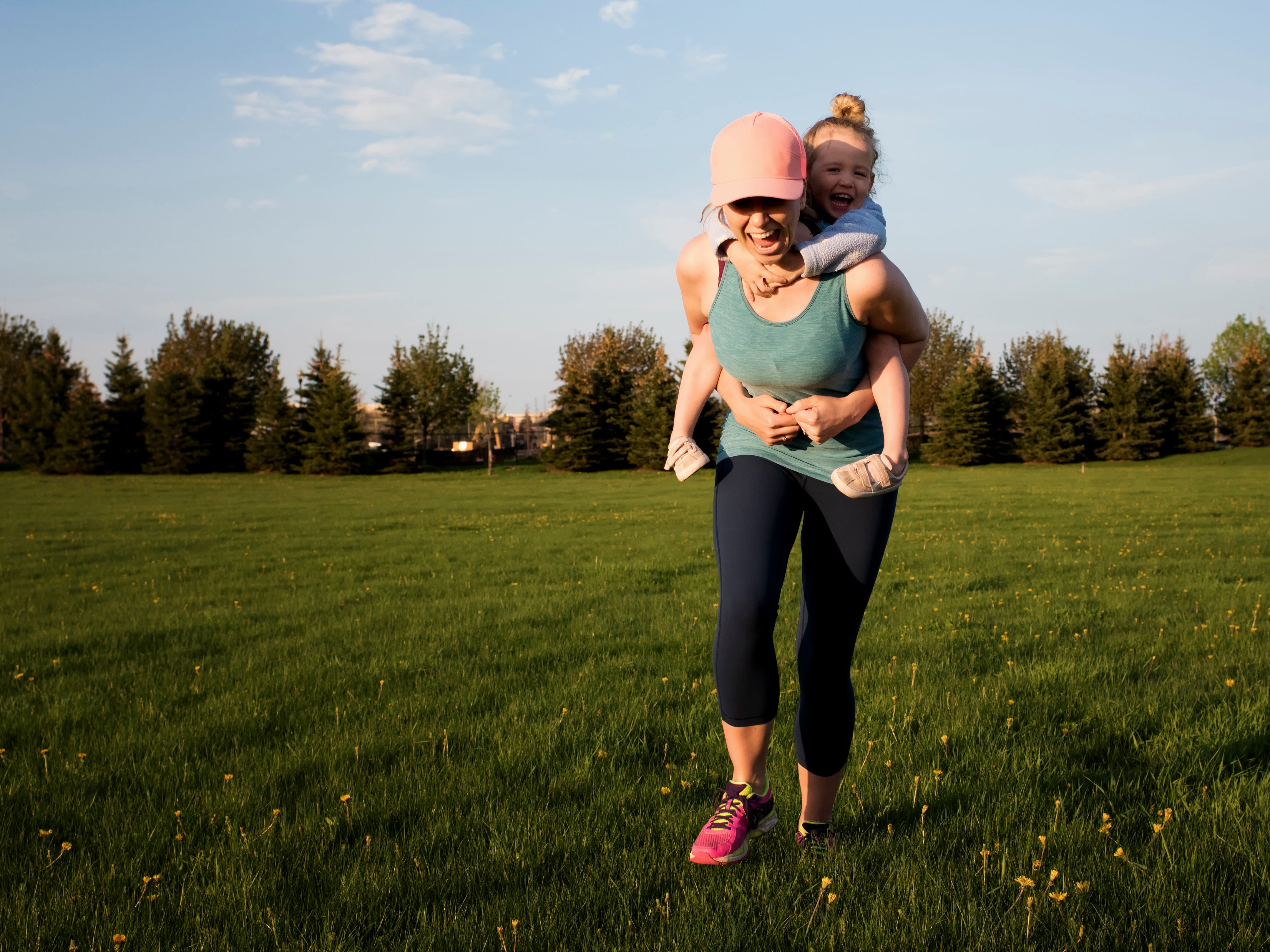 a mother holding her child on her back as they run through a field